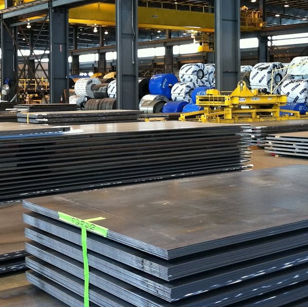 Steel plates and coils stored in an industrial warehouse for manufacturing and construction use.